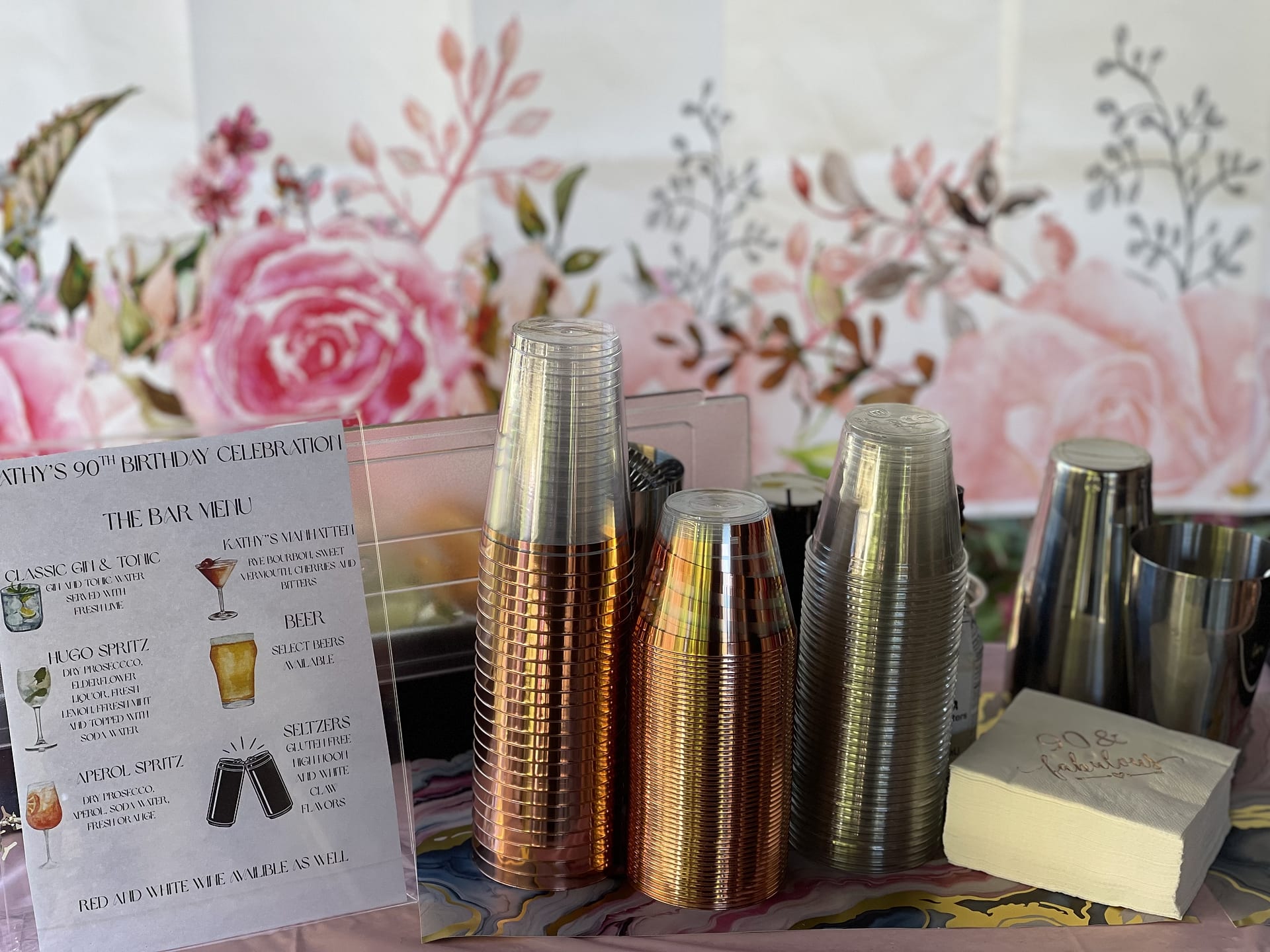A custom printed bar menu beside stacked cups and napkins at an event
